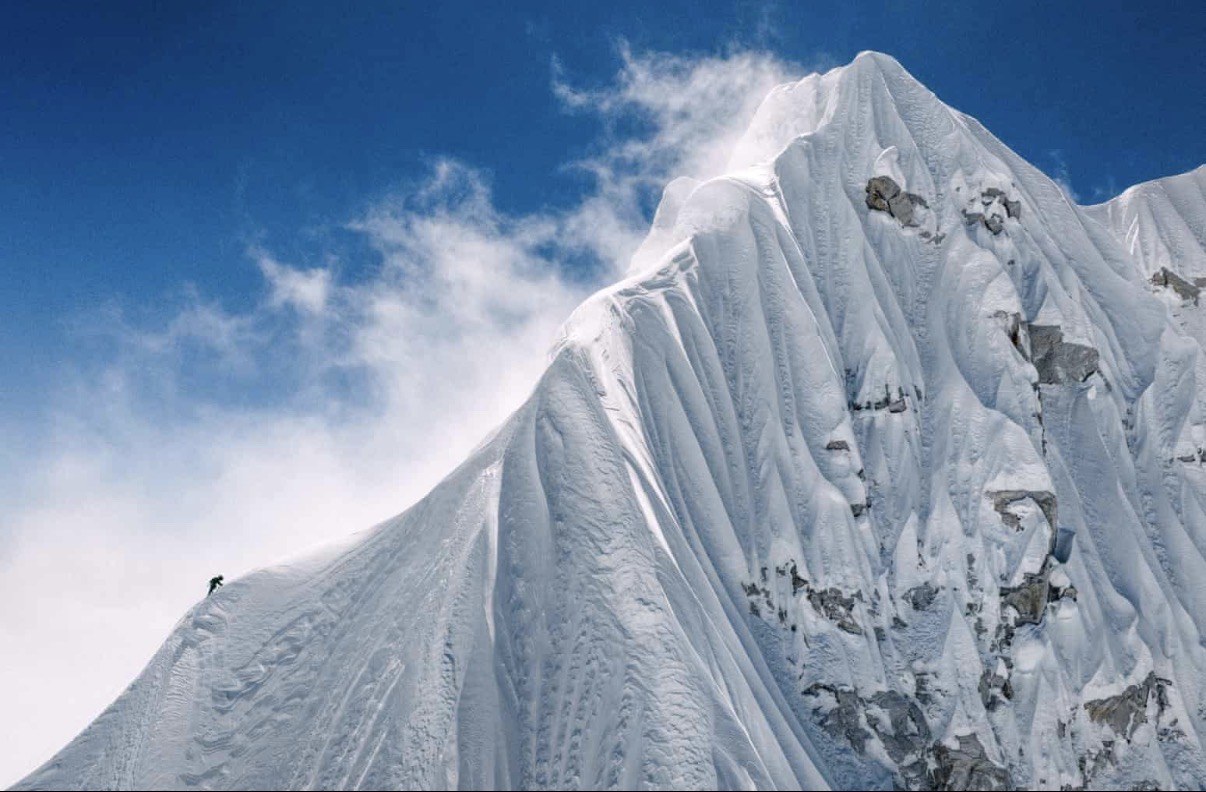 A climber moving below a steep fluted snow and ice face